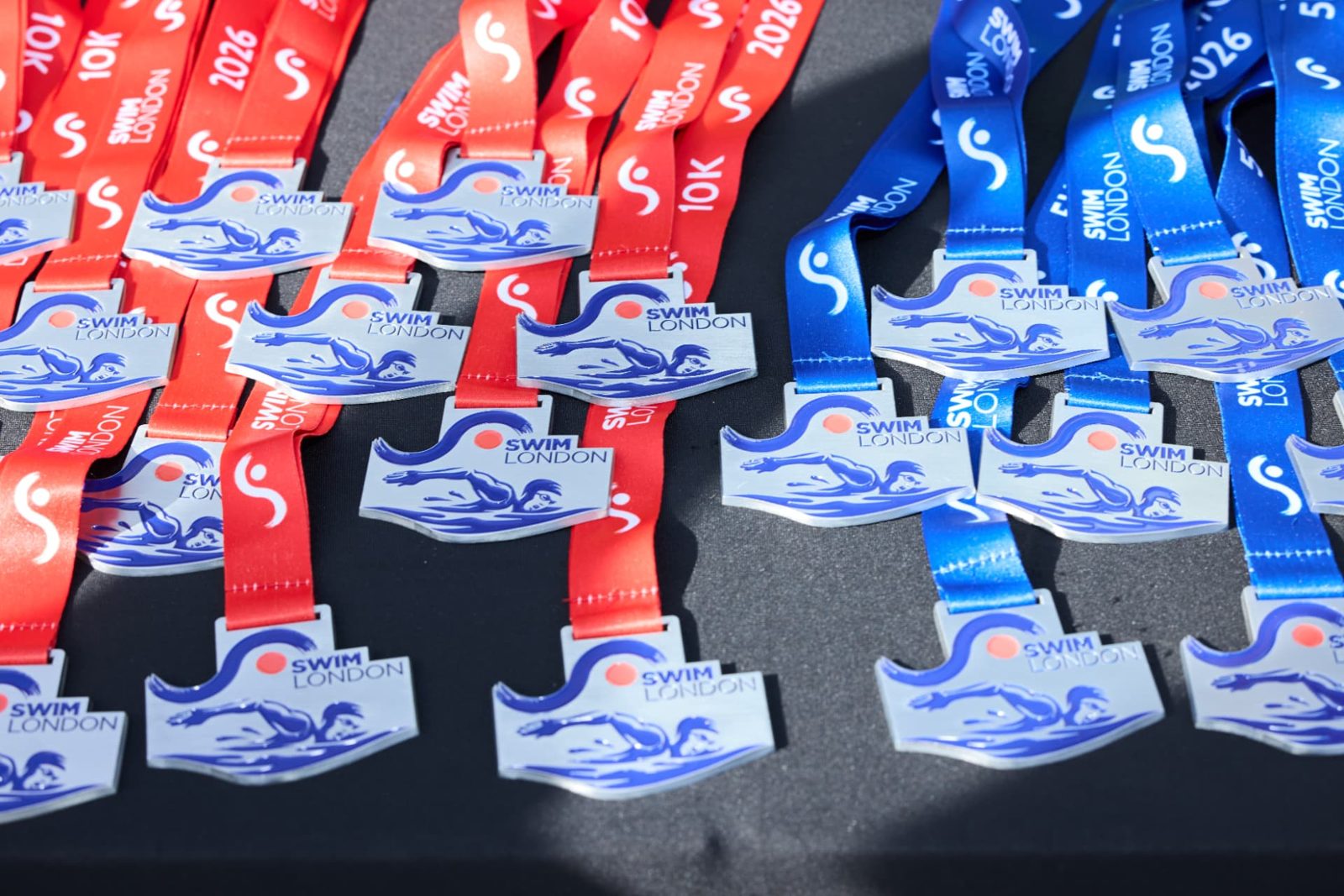 Rows of red 10K and blue 5K Swim London finisher medals laid out before the finish