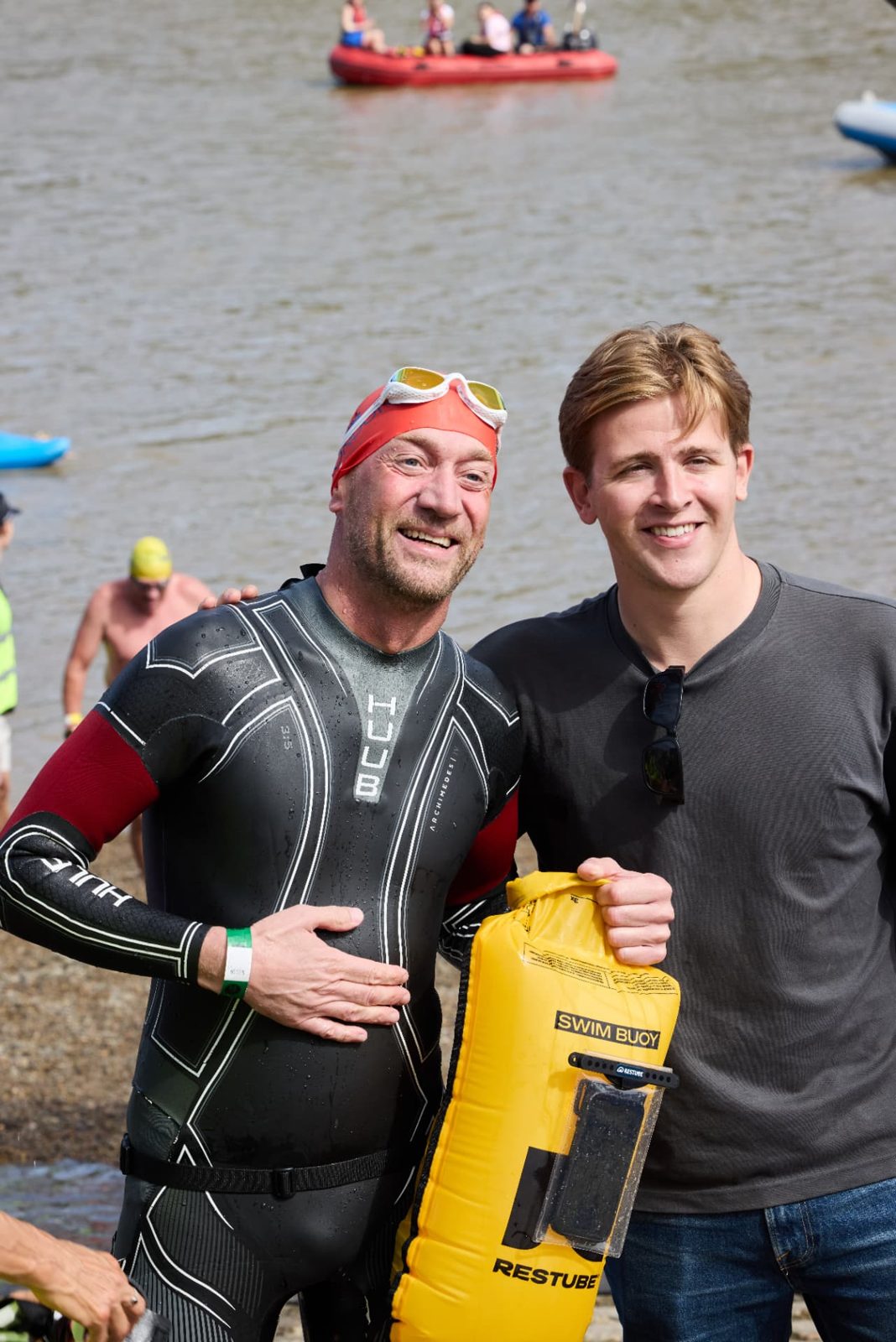 A finisher in a wetsuit with a yellow Restube swim buoy beside a member of the event team