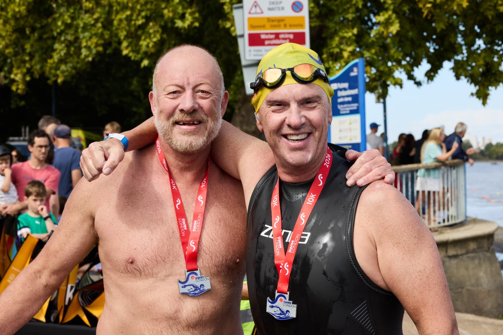 Two finishers arm in arm wearing Swim London 10K medals at Putney Embankment