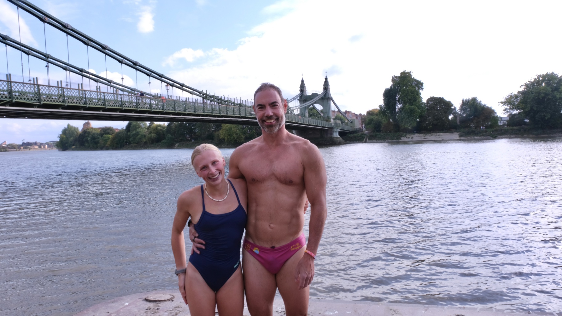Swimmers standing beside the river with Hammersmith Bridge in view