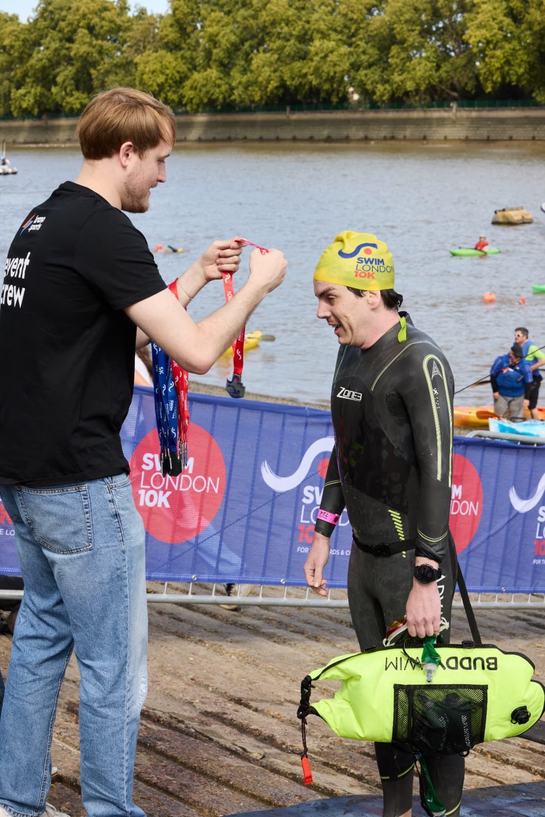 Event crew handing a finisher medal to a swimmer at Putney
