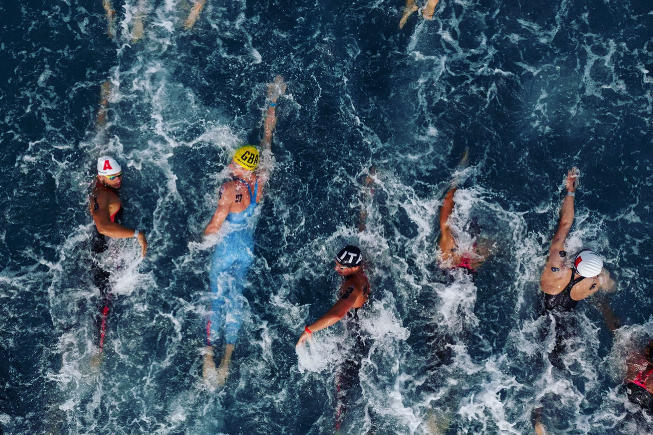 Open-water swimmers stroking through deep blue water from above