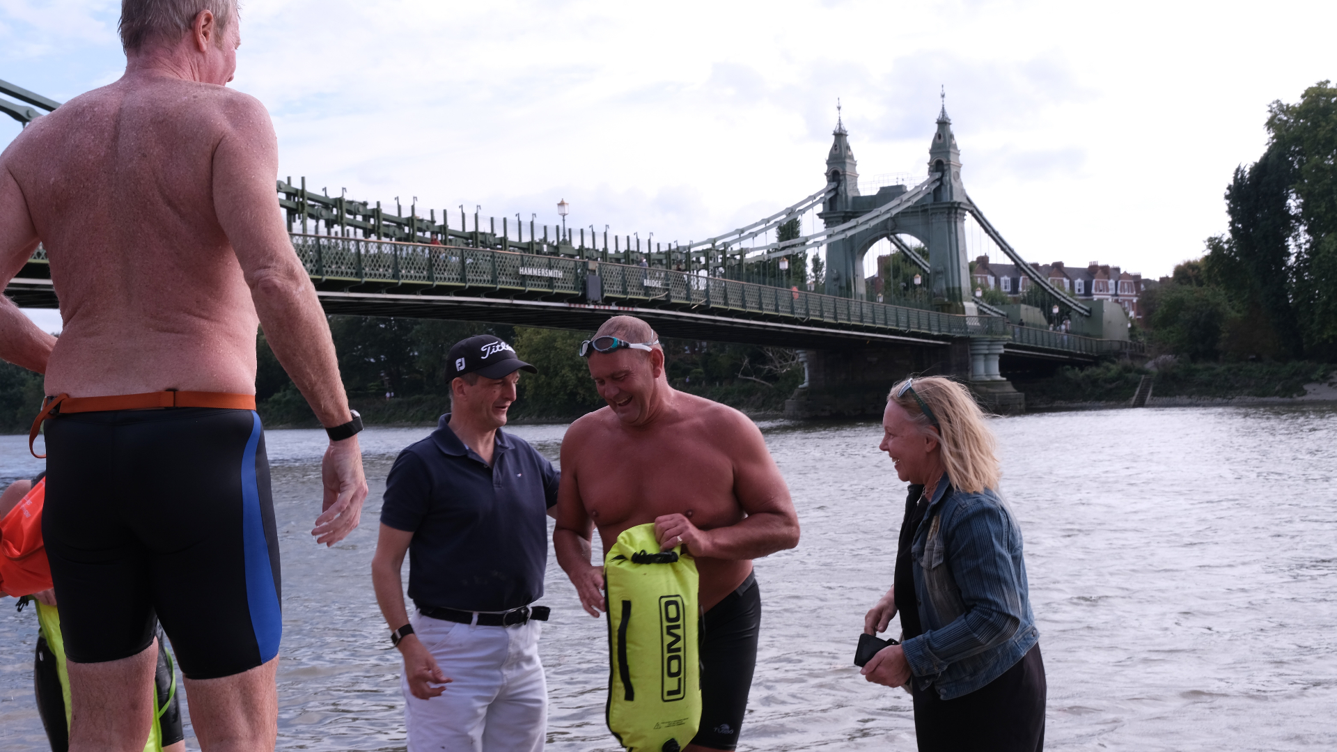 Swimmers and supporters smiling in the Thames beside Hammersmith Bridge