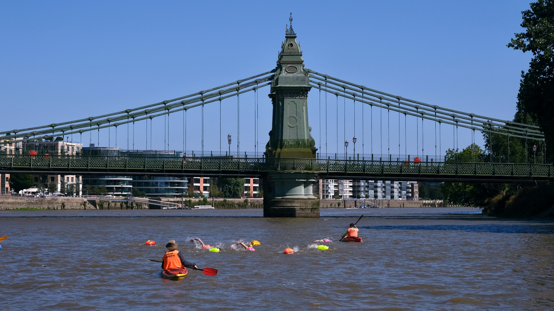 Swimmers escorted by safety kayaks beneath Hammersmith Bridge