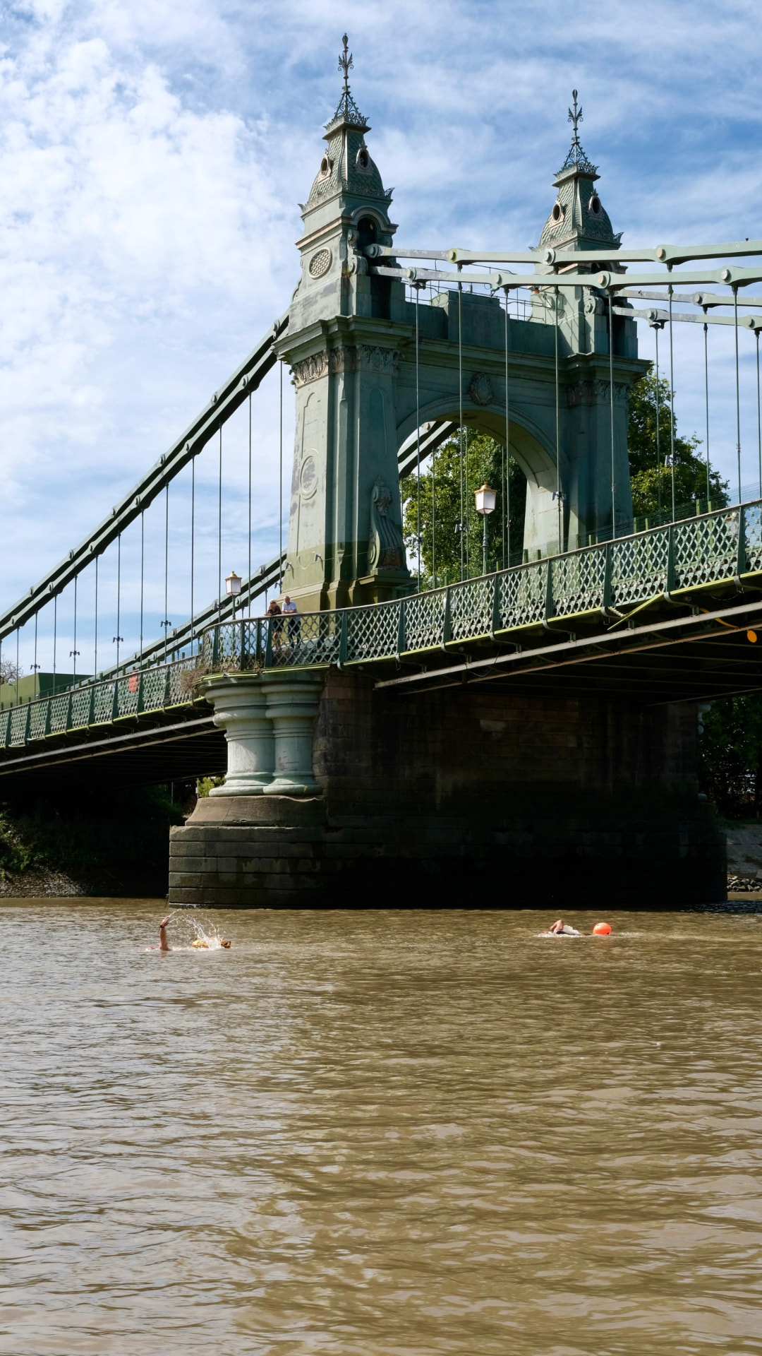 Hammersmith Bridge towering over two swimmers passing underneath