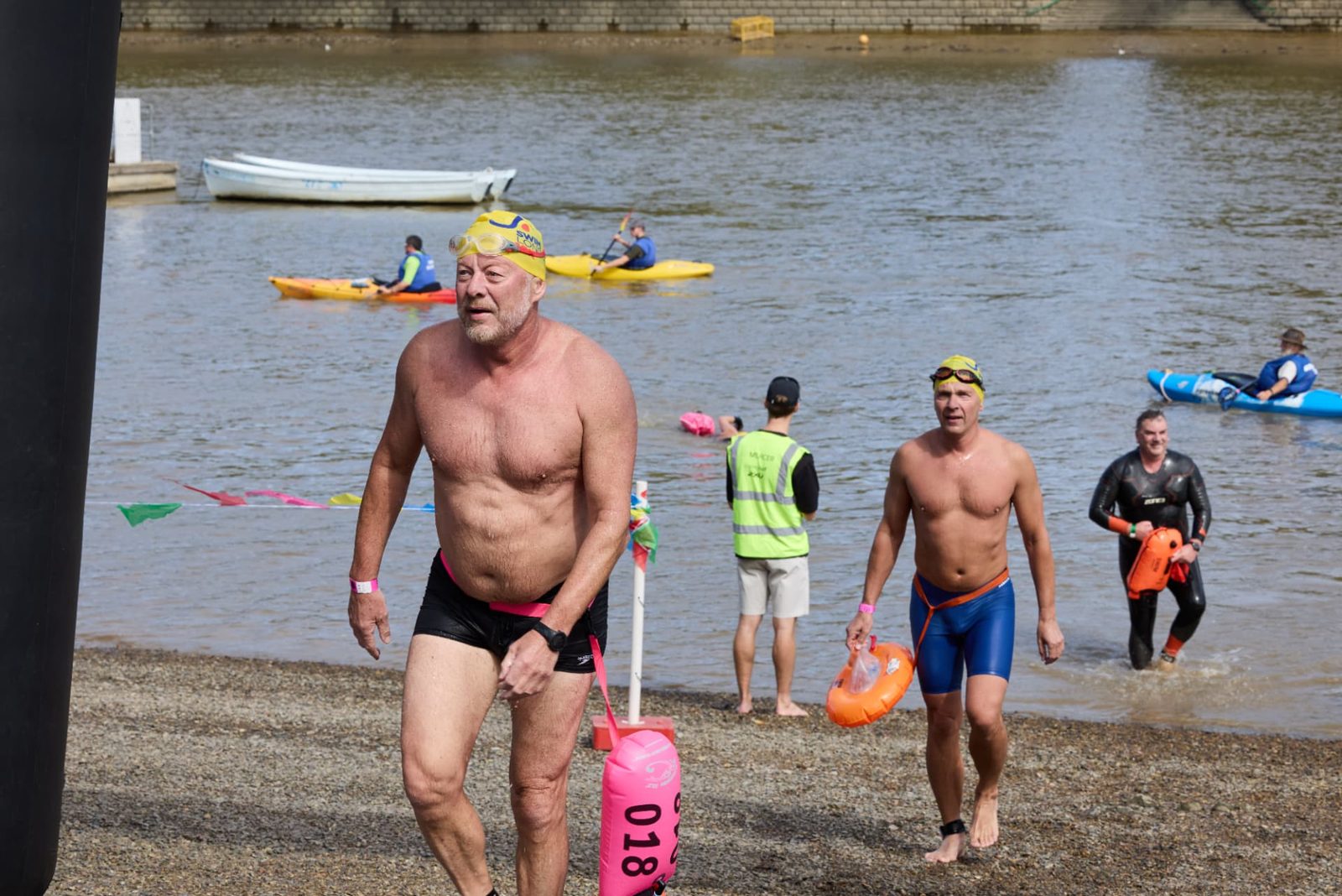 A swimmer walking out of the river onto the foreshore at Putney with his tow float